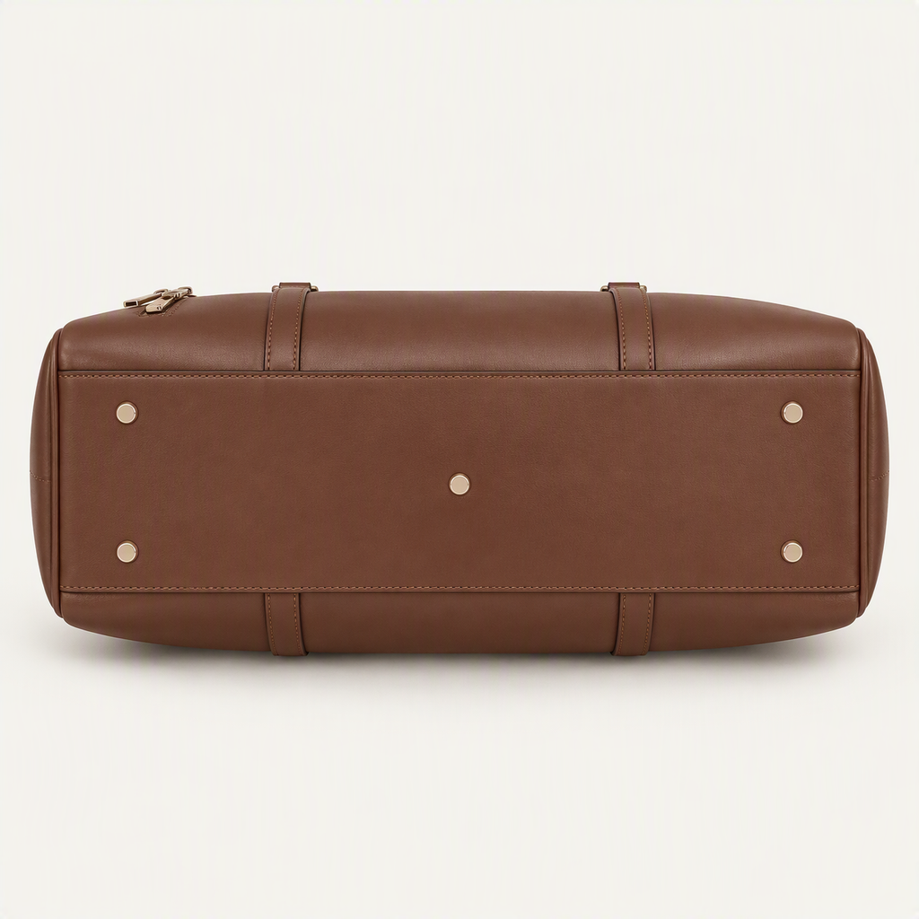 A brown leather duffel bag shown from the bottom, featuring a smooth texture, stitched paneling, and small gold-tone metal studs on a light gray background.