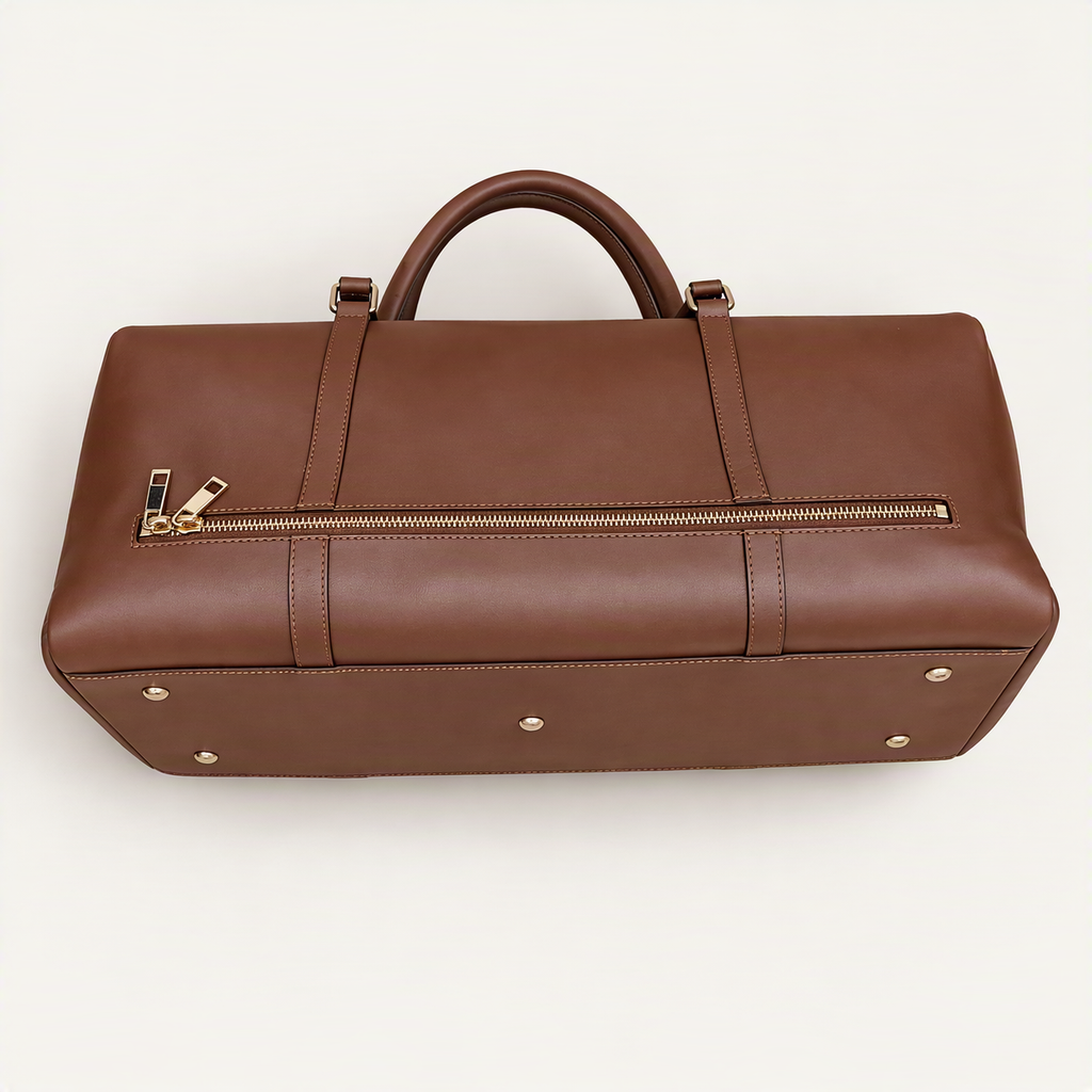 A brown leather duffel bag with a top handle, a horizontal zippered pocket on the front, and gold-tone hardware, photographed on a clean off-white background.