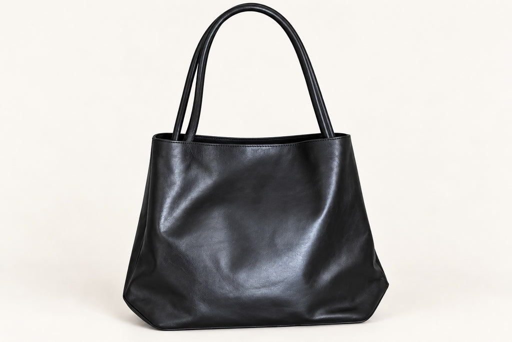A spacious black tote with a softly structured silhouette, long shoulder handles and an elegant gold-tone zipped front pocket. A refined everyday piece combining minimalist design with practical storage.