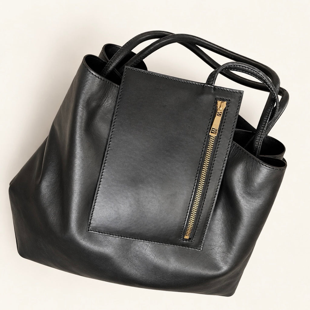 Close-up of the black tote bag, highlighting the large front panel with a vertical gold-tone zip.