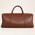 A brown leather duffel bag with double top handles and gold-tone hardware, photographed against a clean, light beige background.